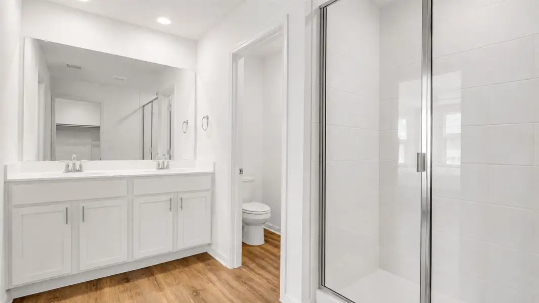 A pristine bathroom featuring a double vanity, a modern glass shower, and a private toilet alcove. A pristine bathroom featuring a double vanity, a modern glass shower, and a private toilet alcove.