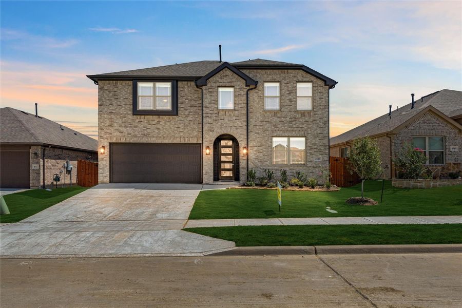 Two-story brick home with arched front door, two-car garage, and manicured lawn at dusk