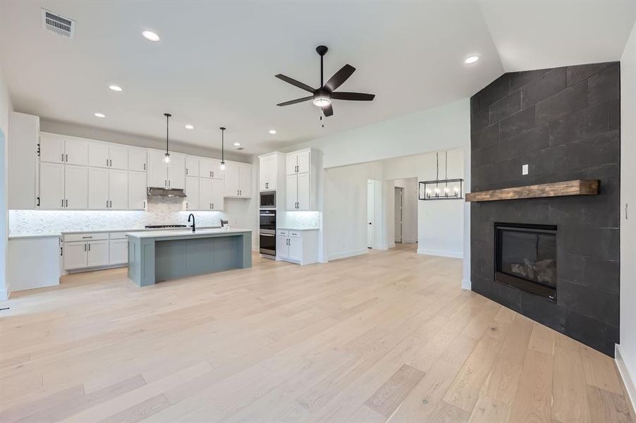 Kitchen with light hardwood / wood-style floors, a tiled fireplace, a center island with sink, white cabinets, and hanging light fixtures