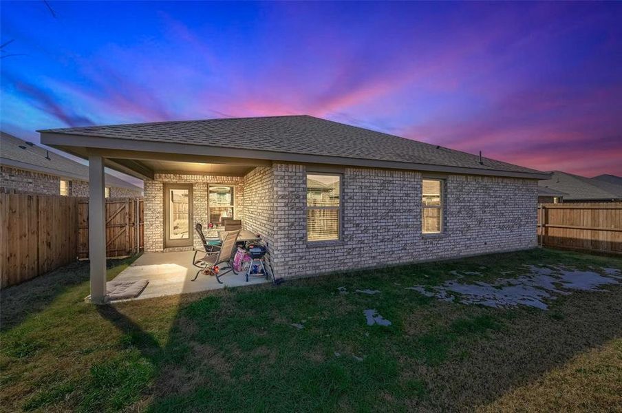 Back house at dusk featuring a patio area and a lawn