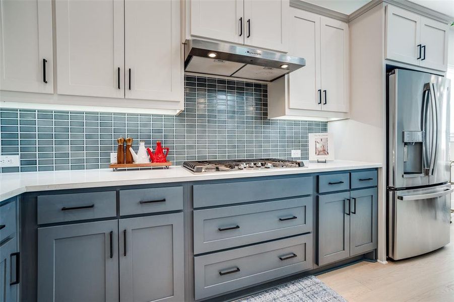 Two tone kitchen featuring dual tone cabinets, stainless steel appliances, tasteful backsplash, and light stone counters