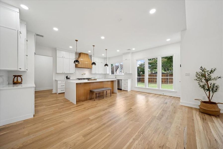 Kitchen featuring white cabinets, a center island, premium range hood, light hardwood / wood-style floors, and a kitchen breakfast bar