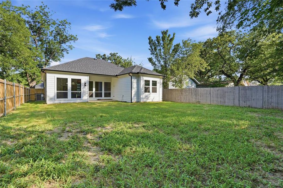 Expansive backyard featuring a new construction home with white siding, a dark shingle roof, and a privacy fence Expansive backyard featuring a new construction home with white siding, a dark shingle roof, and a privacy fence