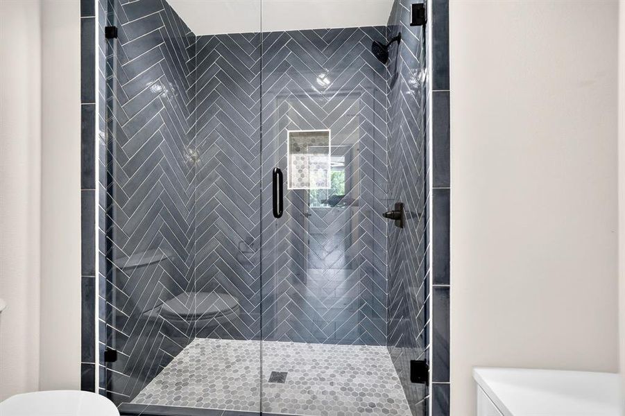 Spa-inspired walk-in shower with stylish herringbone tile, mosaic floor, and frameless glass door. Spa-inspired walk-in shower with stylish herringbone tile, mosaic floor, and frameless glass door.