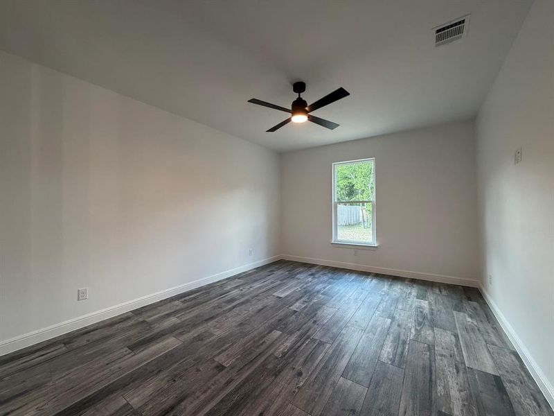 Spacious room featuring wood-finish flooring, a modern black ceiling fan with integrated lighting, white baseboards, and a bright window with a backyard view