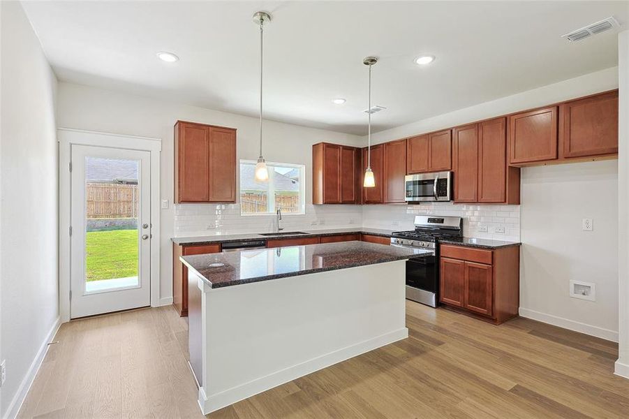 Kitchen featuring sink, a kitchen island, light hardwood / wood-style flooring, stainless steel appliances, and dark stone counters