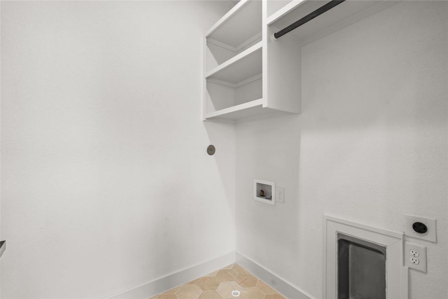 The dedicated laundry room features custom white cabinets, built-in shelving, and a hanging drying rod. The utility wall includes washer and dryer hookups with heavy-duty outlets, all set against an easy-to-clean, geometric tile floor.
