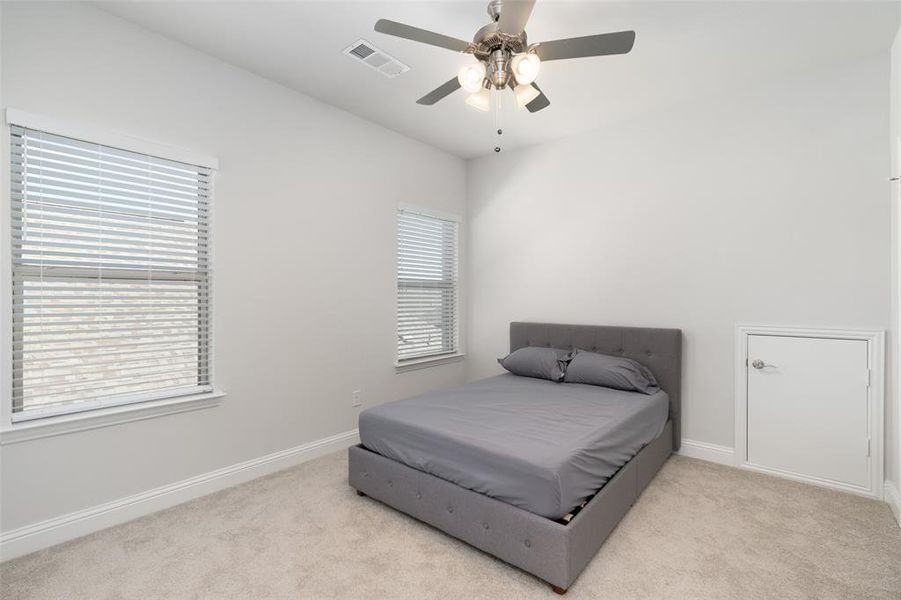 Carpeted bedroom featuring multiple windows and ceiling fan