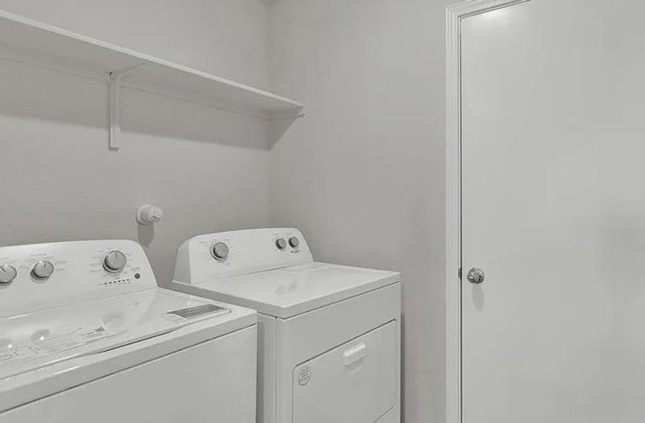Dedicated laundry area featuring a white wall shelf, a white painted door with a chrome doorknob, and light gray wall finishes Dedicated laundry area featuring a white wall shelf, a white painted door with a chrome doorknob, and light gray wall finishes