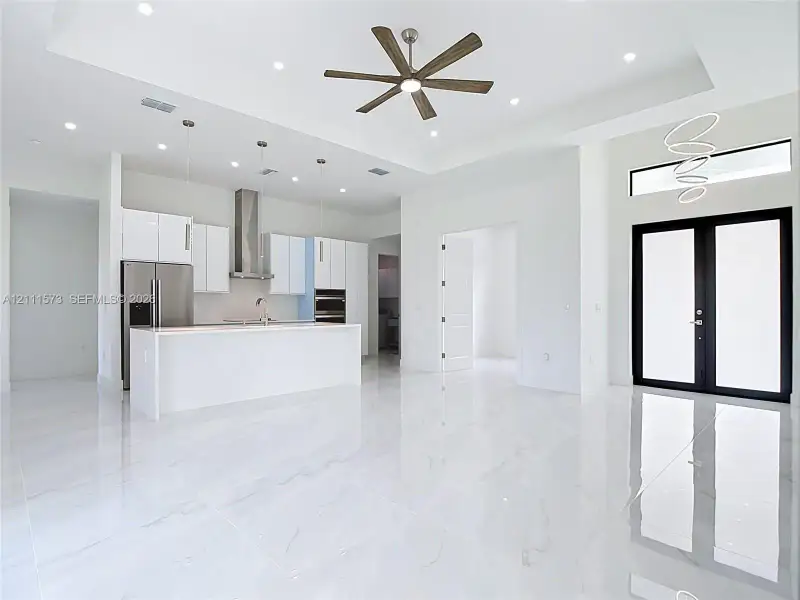 Open-concept kitchen featuring white cabinetry, a center island, stainless steel appliances, recessed ceiling lighting, and polished stone-finish flooring throughout