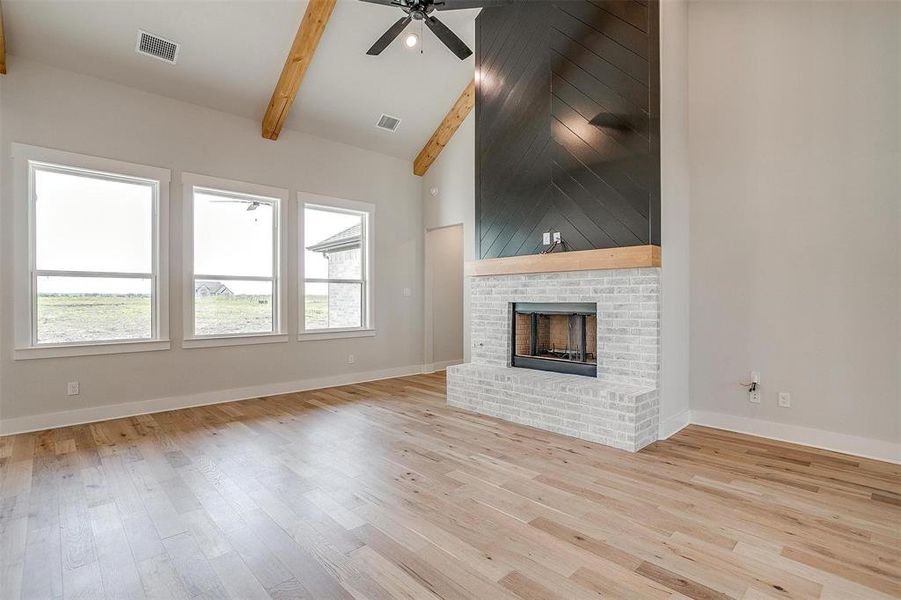 Unfurnished living room with vaulted ceiling with beams, a brick fireplace, light wood-type flooring, and ceiling fan