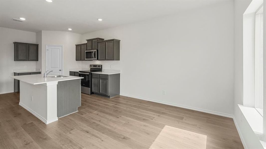 The open-concept kitchen features dark grey cabinetry, stainless steel appliances, and a central island with a sink and white countertop