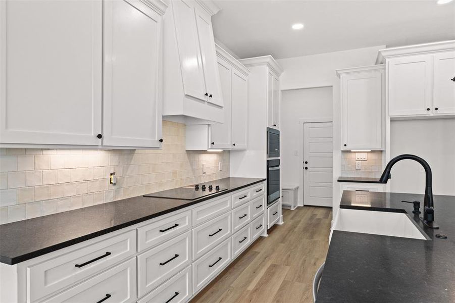 Kitchen featuring white cabinetry, dark stone counters, light wood-style floors, and recessed lighting