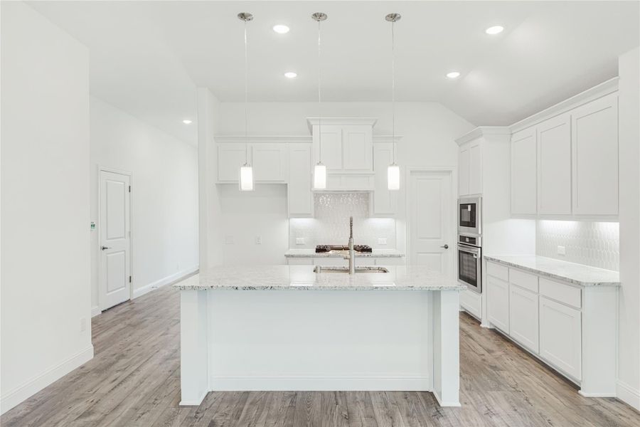 White kitchen with large center island, granite countertops, pendant lights, and stainless steel double ovens White kitchen with large center island, granite countertops, pendant lights, and stainless steel double ovens