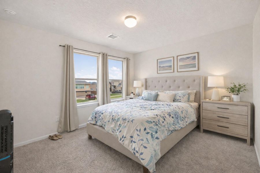 Bright upstairs bedroom with plush carpet, neutral palette, and large windows framing neighborhood views.