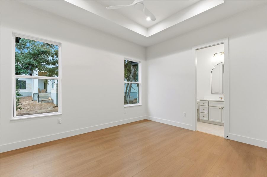 Unfurnished bedroom featuring light wood-style floors, ceiling fan, ensuite bathroom, a tray ceiling, and recessed lighting