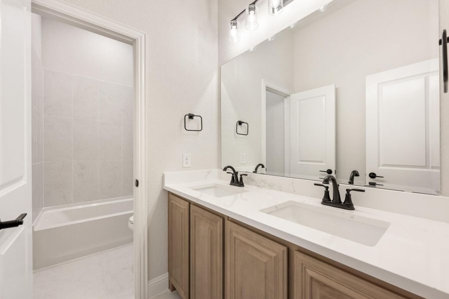 Bathroom with double sink vanity, white quartz countertop, wood cabinets, and a bathtub with tiled surround