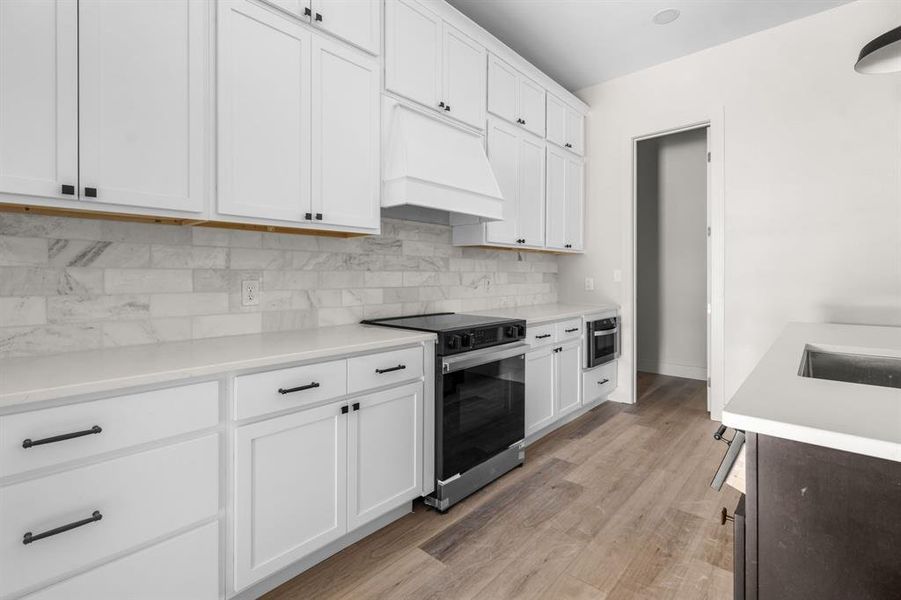 Kitchen with range with electric stovetop, custom range hood, white cabinetry, and tasteful backsplash