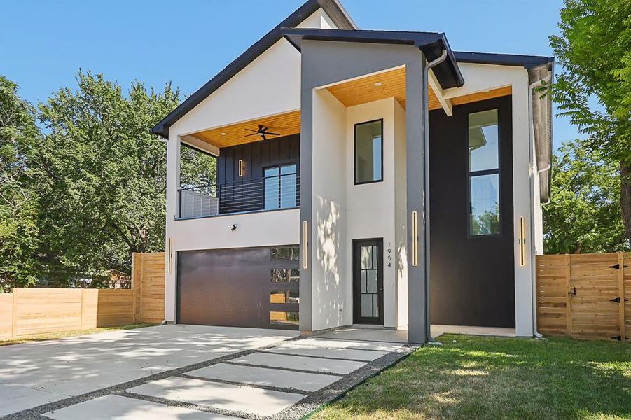 Modern home with a balcony, an attached garage, concrete driveway, stucco siding, and a ceiling fan