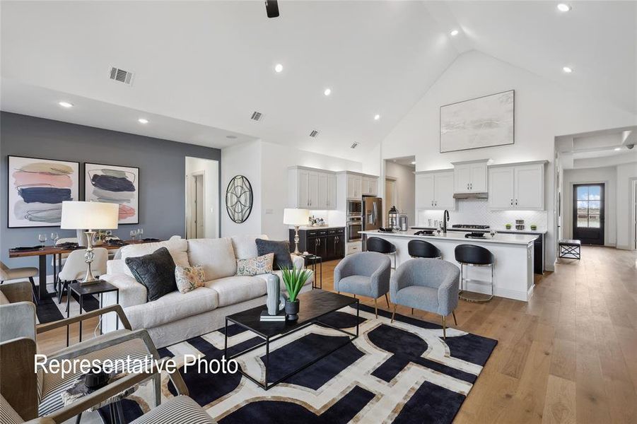 Open-concept living space featuring vaulted ceilings, wood-finish flooring, a kitchen island with seating, pendant lighting, and recessed ceiling lights
