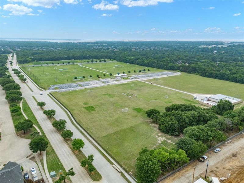 Expansive green spaces including multiple sports fields and a large parking area, bordered by a tree-lined thoroughfare