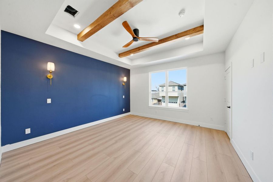 This room features a contemporary design with a striking navy accent wall, elegant wall sconces, light wood flooring, and a ceiling with exposed wood beams and a modern fan. A large window provides natural light and a view of the neighborhood.