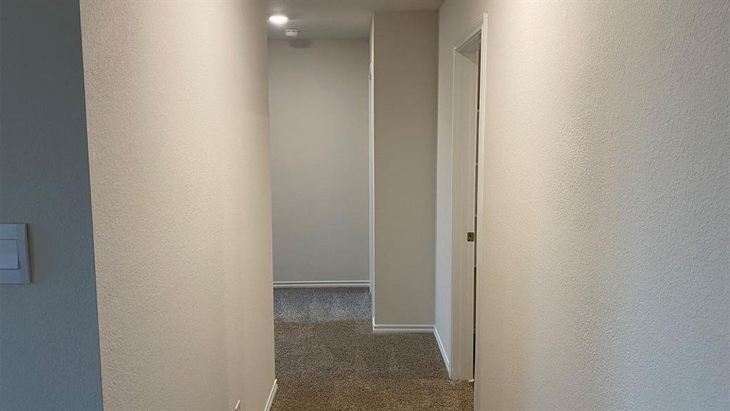 Hallway with dark colored carpet and a textured wall