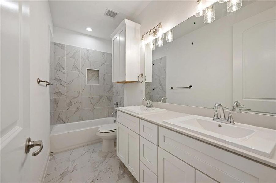 Full bathroom featuring vanity, tiled shower / bath combo, and toilet