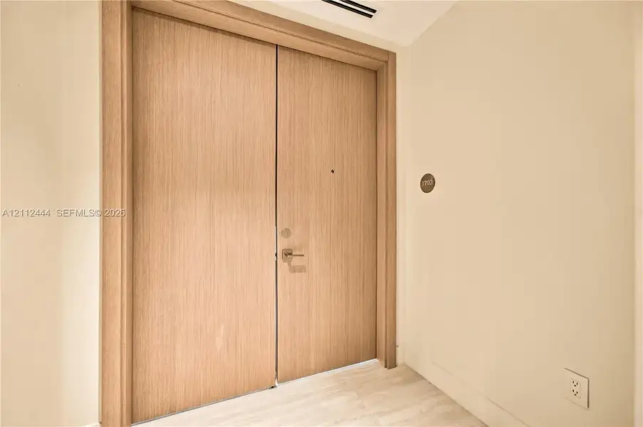 Double-door entry featuring light wood-finish slab doors with matching door casing and metallic hardware