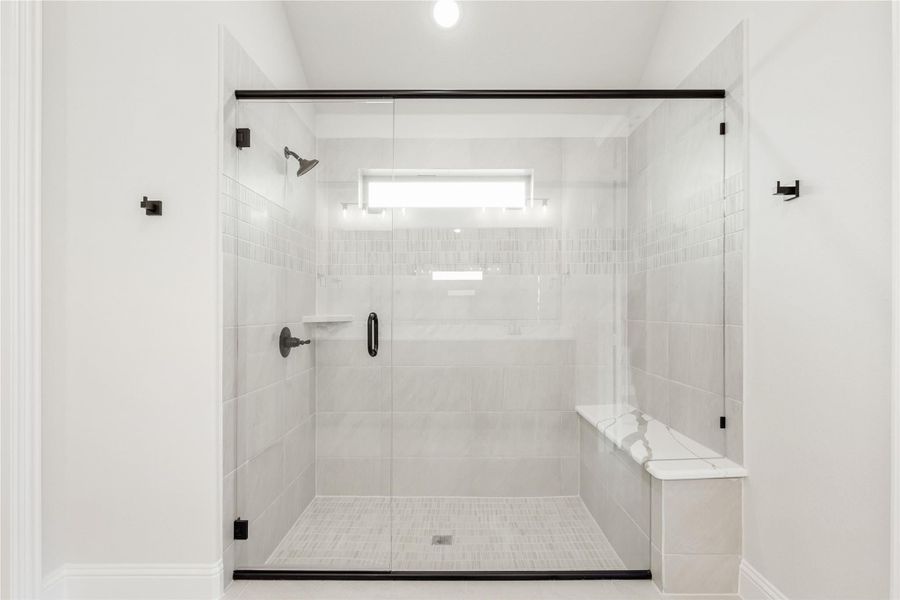 Walk-in shower with glass door, white marble tile walls, built-in bench, and black hardware fixtures