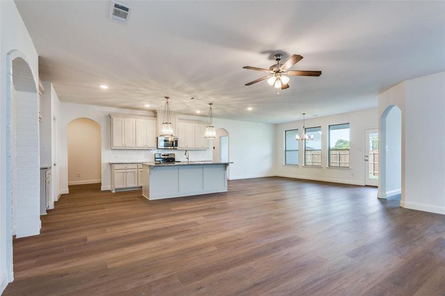 Kitchen with ceiling fan with notable chandelier, stainless steel appliances, dark hardwood / wood-style flooring, pendant lighting, and a kitchen island with sink