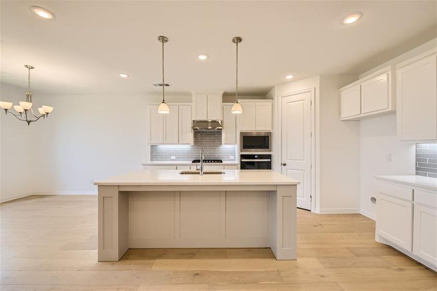 Kitchen with light hardwood / wood-style flooring, an island with sink, stainless steel microwave, backsplash, and oven