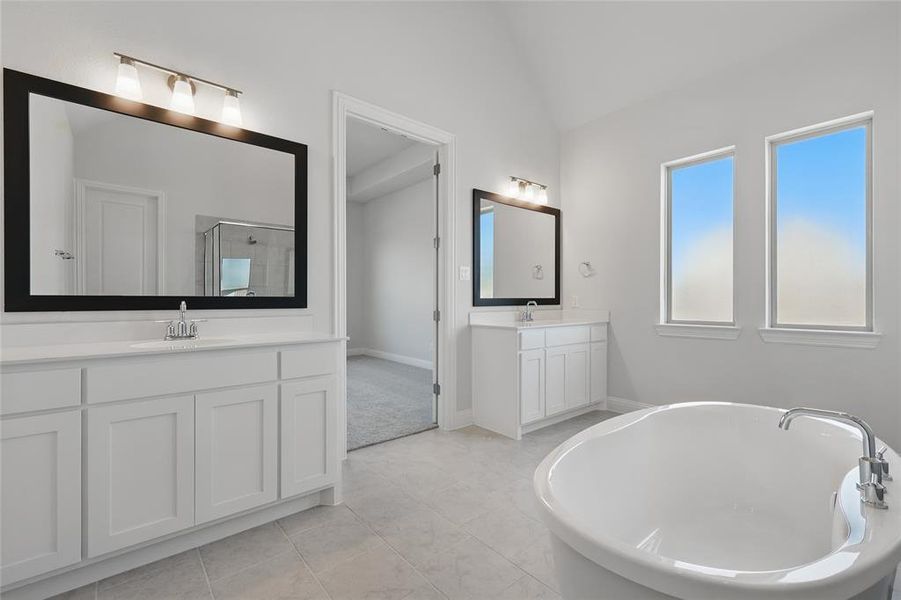 Bathroom featuring two vanities, lofted ceiling, a soaking tub, a shower stall, and light tile patterned floors