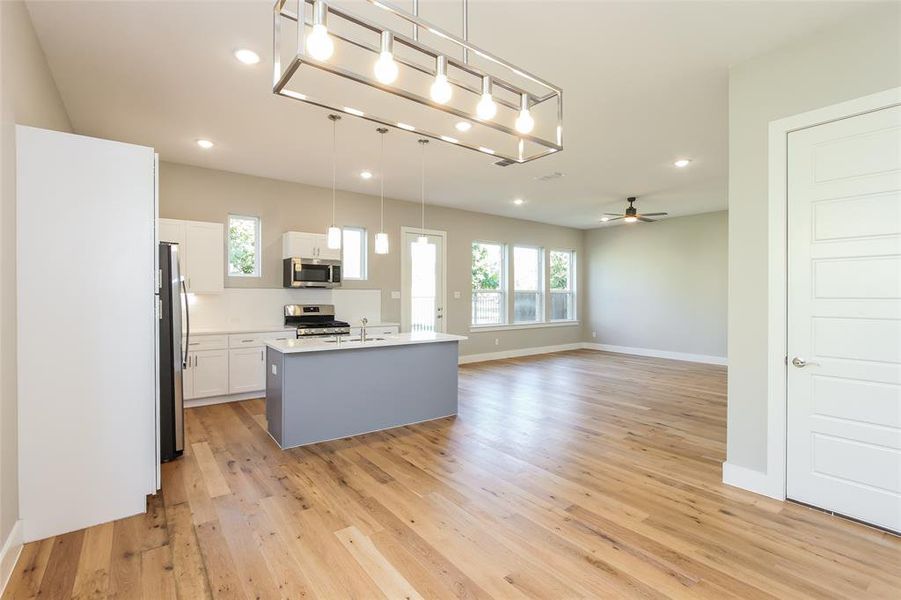 Kitchen featuring decorative light fixtures, white cabinetry, stainless steel appliances, a center island with sink, and light hardwood / wood-style flooring