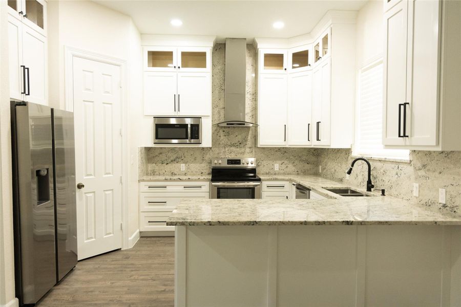 Kitchen featuring glass insert cabinets, light stone counters, stainless steel appliances, a peninsula, and white cabinetry