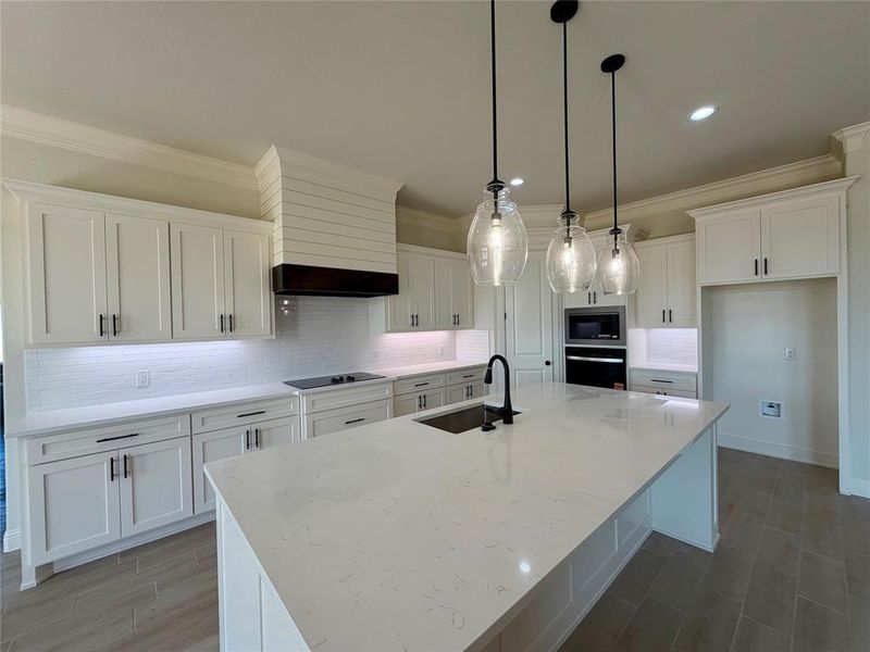 Kitchen featuring white cabinets, tasteful backsplash, a large island with sink, light stone countertops, and crown molding Kitchen featuring white cabinets, tasteful backsplash, a large island with sink, light stone countertops, and crown molding