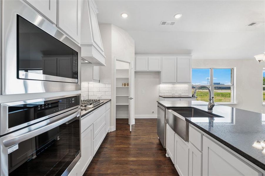 Kitchen with appliances with stainless steel finishes, white cabinets, dark stone counters, dark wood finished floors, and recessed lighting Kitchen with appliances with stainless steel finishes, white cabinets, dark stone counters, dark wood finished floors, and recessed lighting