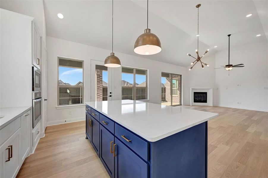 Kitchen featuring two tone cabinets, light wood finished floors, a fireplace, vaulted ceiling, and a kitchen island Kitchen featuring two tone cabinets, light wood finished floors, a fireplace, vaulted ceiling, and a kitchen island
