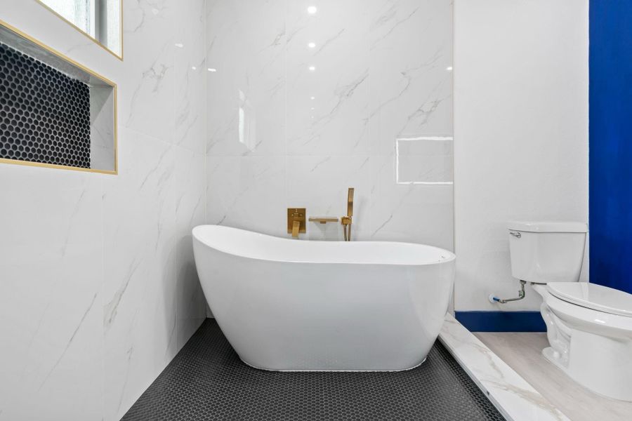 This primary baths features a freestanding tub with elegant gold fixtures,