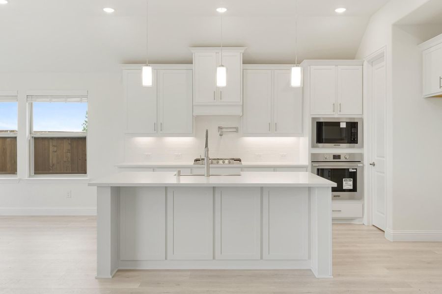 White kitchen with large center island, pendant lights, white cabinets, and stainless steel built-in oven and microwave