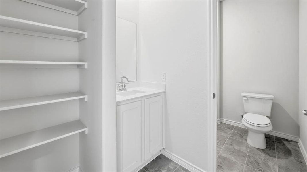 Powder room featuring a white vanity with integrated sink, mounted mirror, and a toilet with tile flooring