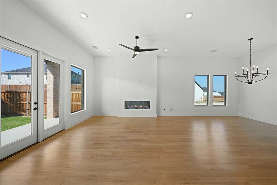 Unfurnished living room featuring light wood-type flooring, recessed lighting, a glass covered fireplace, a ceiling fan, and a chandelier Unfurnished living room featuring light wood-type flooring, recessed lighting, a glass covered fireplace, a ceiling fan, and a chandelier