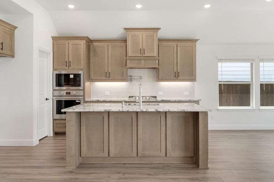Kitchen with tan wood cabinets, granite island, stainless steel appliances, and light hardwood floors Kitchen with tan wood cabinets, granite island, stainless steel appliances, and light hardwood floors