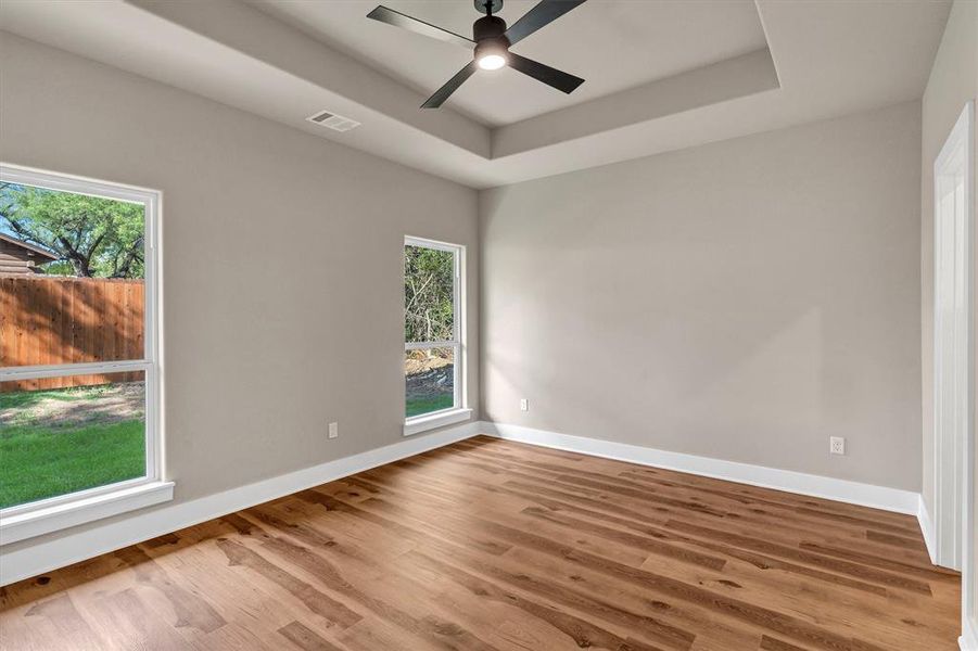 Spare room with a raised ceiling, wood finished floors, and a ceiling fan Spare room with a raised ceiling, wood finished floors, and a ceiling fan