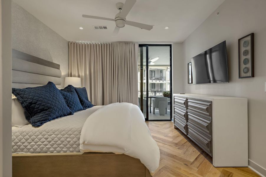 Herringbone hardwood floors add warmth and texture to this comfortable bedroom, featuring direct balcony access for private outdoor enjoyment.