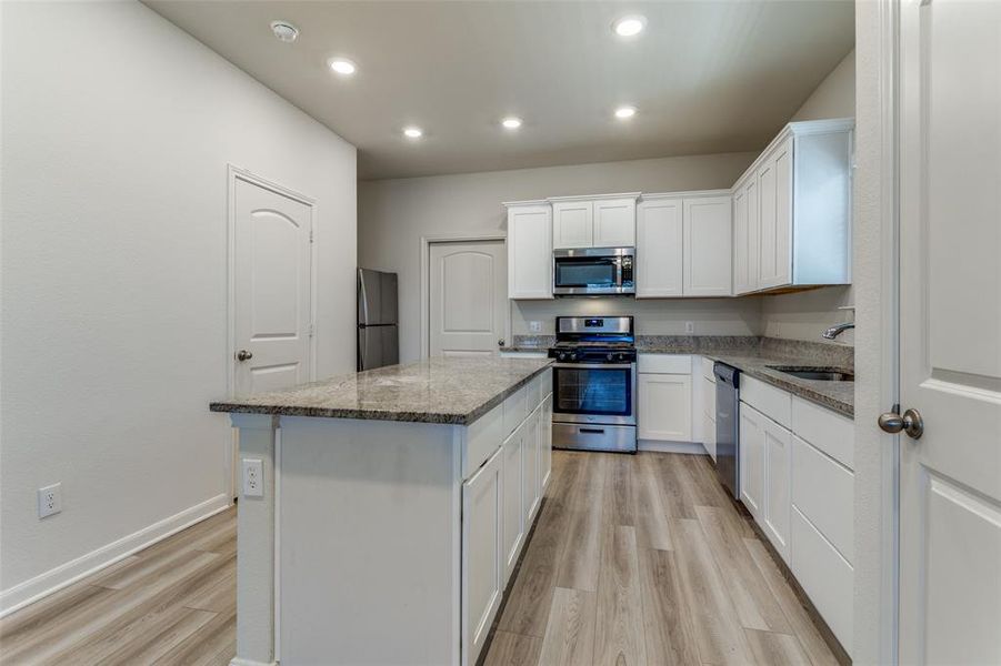 Kitchen featuring appliances with stainless steel finishes, white cabinets, light hardwood / wood-style floors, light stone countertops, and a center island