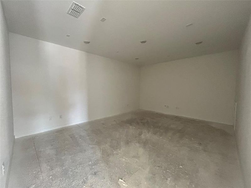 The empty media room is a vast, open space with blank walls and an open floor plan, awaiting the addition of a large screen, seating, and entertainment equipment to transform it into a cozy viewing area.