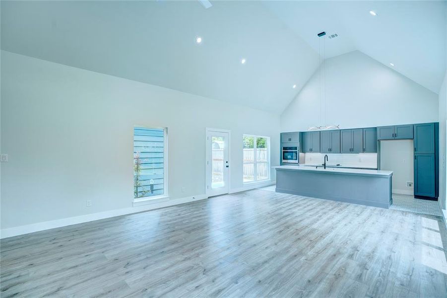 Open-concept living space featuring wood-finish flooring, a vaulted ceiling, recessed lighting, a kitchen island with a quartz countertop, and grey cabinetry