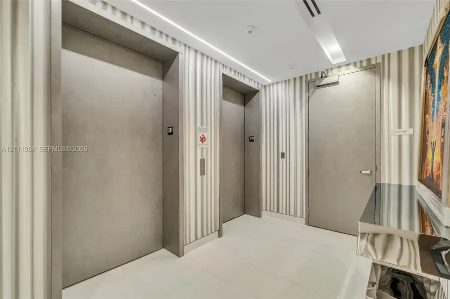 Elevator foyer featuring dual elevator doors with matte grey finish, full-height striped wall coverings, recessed ceiling lighting, and large-format tile flooring Elevator foyer featuring dual elevator doors with matte grey finish, full-height striped wall coverings, recessed ceiling lighting, and large-format tile flooring