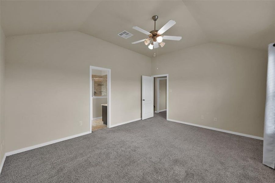 This is a spacious, well-lit room featuring vaulted ceilings, a ceiling fan, plush carpeting, and neutral walls.